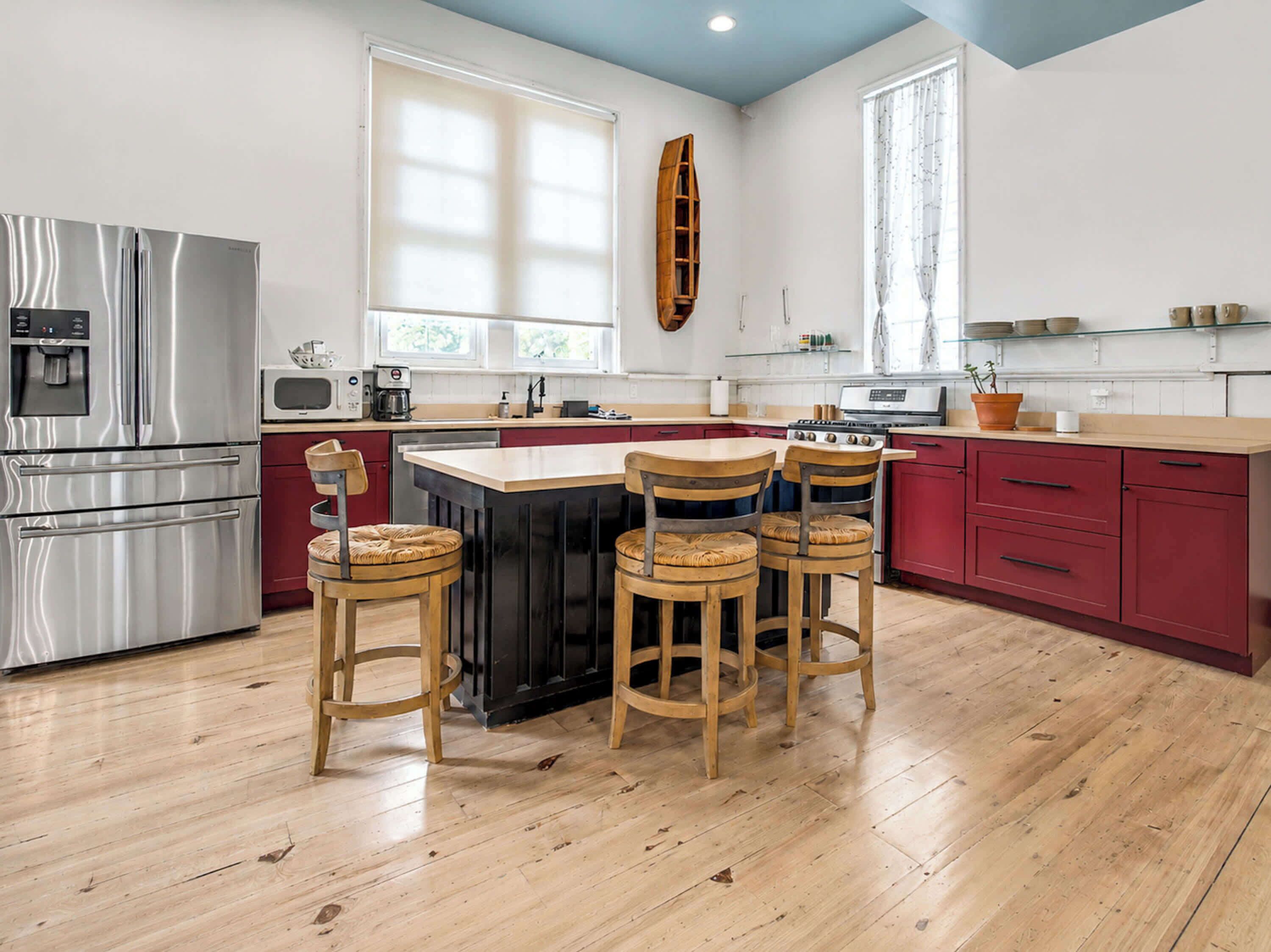 A modern kitchen with a central island, wooden chairs, stainless steel appliances, and a red cabinetry.