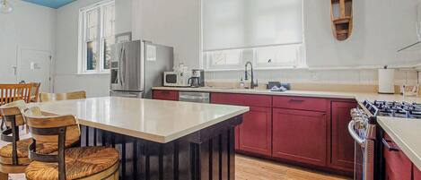 A kitchen with a central island, wooden chairs, a refrigerator, a microwave, and a stove.