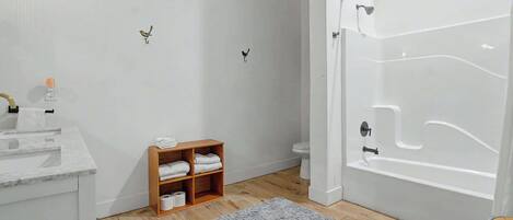 A bathroom with a bathtub, toilet, and a wooden shelf with towels.