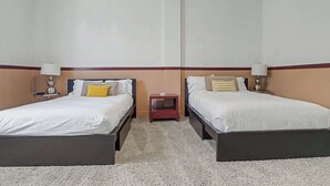 Ein Hotelzimmer mit zwei Einzelbetten, jeweils mit Nachttisch und Lampe, und einem kleinen Tisch dazwischen.
