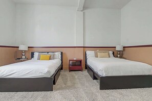 Ein Hotelzimmer mit zwei Einzelbetten, jeweils mit Nachttisch und Lampe, und einem kleinen Tisch dazwischen.