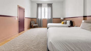A hotel room with two beds, a chair, a desk, and a ceiling fan.