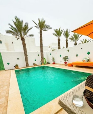 A swimming pool with a tiled deck, surrounded by palm trees and potted plants.