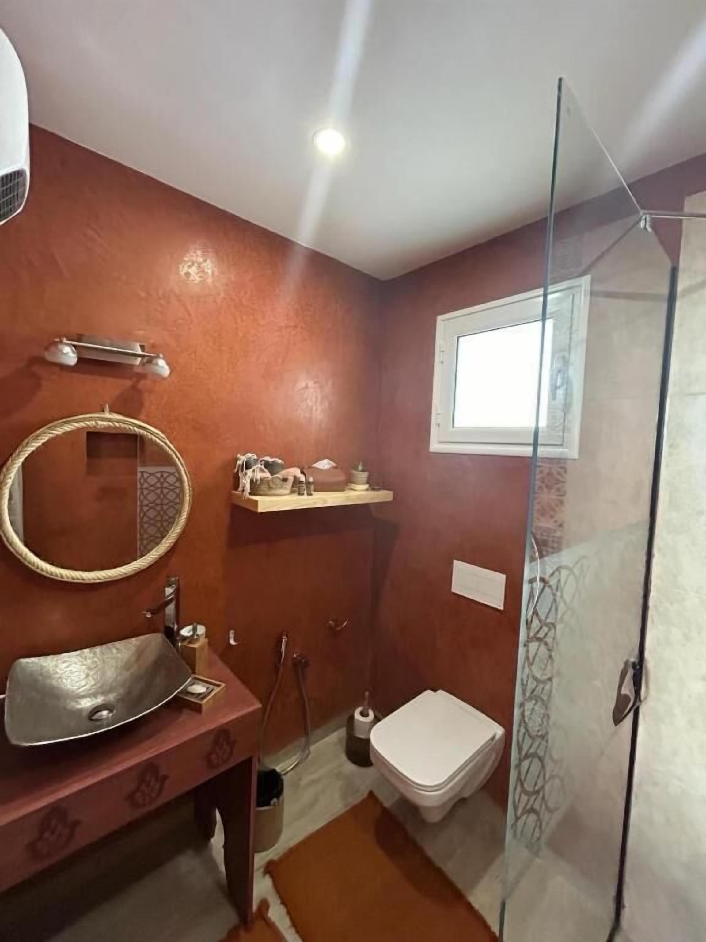 Een badkamer met een ronde spiegel, een wastafel, toilet en douche.