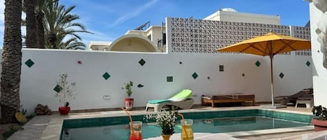 A poolside area with lounge chairs, a table with drinks, and a decorative wall.