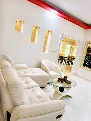 A modern living room with a sectional sofa, a glass coffee table, and a dining area in the background.