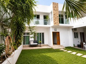 A modern two-story house with a balcony, a front door, and a small patio area with a chair and table.