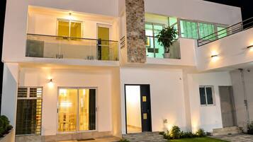 A modern two-story house with a balcony, large windows, and a well-lit entrance.