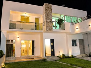 A modern two-story house with a balcony, large windows, and a well-lit entrance.