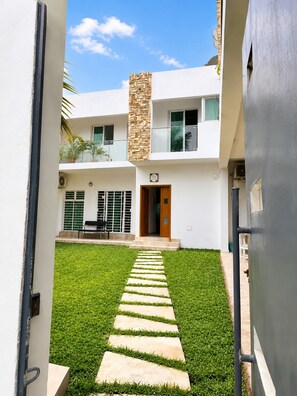 A modern two-story building with a stone accent wall, a paved pathway leading to the entrance, and a small outdoor seating area. - Beautiful 5 bedrooms Villa in charming Abidjan (Abidjan)