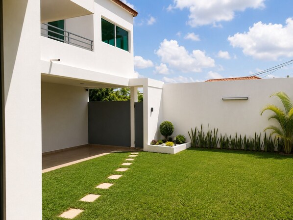 A modern two-story house with a flat roof, a covered patio, and a well-maintained lawn with stepping stones.
