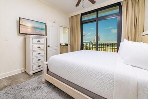 Ein Schlafzimmer mit einem großen Bett, einem Fernseher auf einer Kommode, einem Fenster mit Blick auf Gebäude und einem Balkon.
