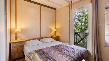 A bedroom with a bed, two bedside lamps, a wooden nightstand, and a view through a door to an outdoor balcony.