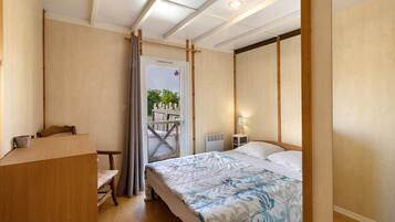 Een slaapkamer met een bed, een bureau, een stoel, een radiator en een raam met uitzicht op groen.