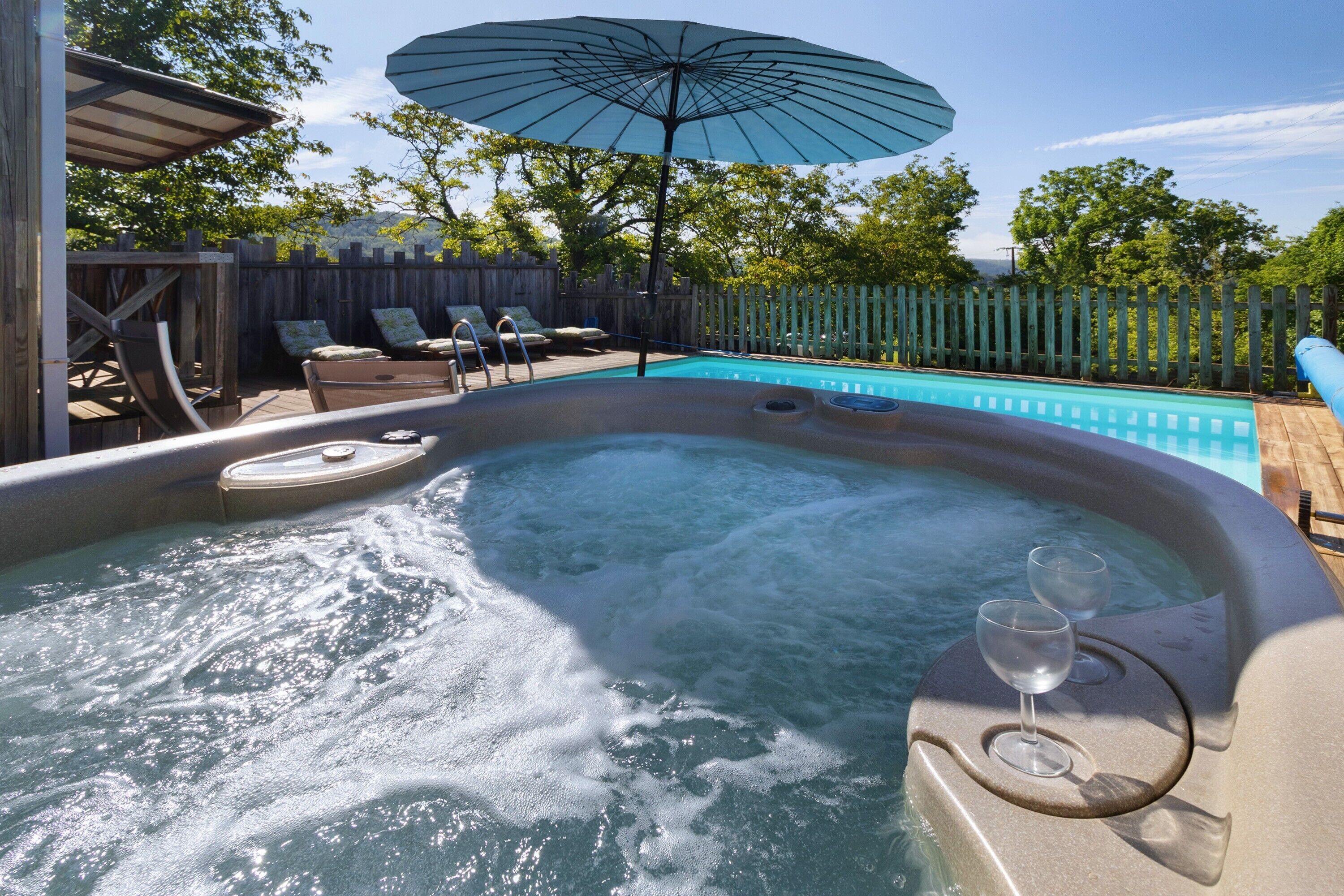 Een hottub met een glas en een lounge stoel, omgeven door een houten terras en een zwembad.