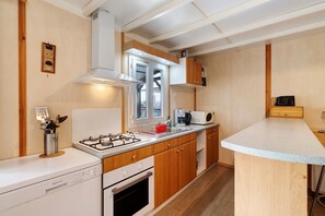 A compact kitchen with a gas stove, oven, wooden cabinets, and a microwave.