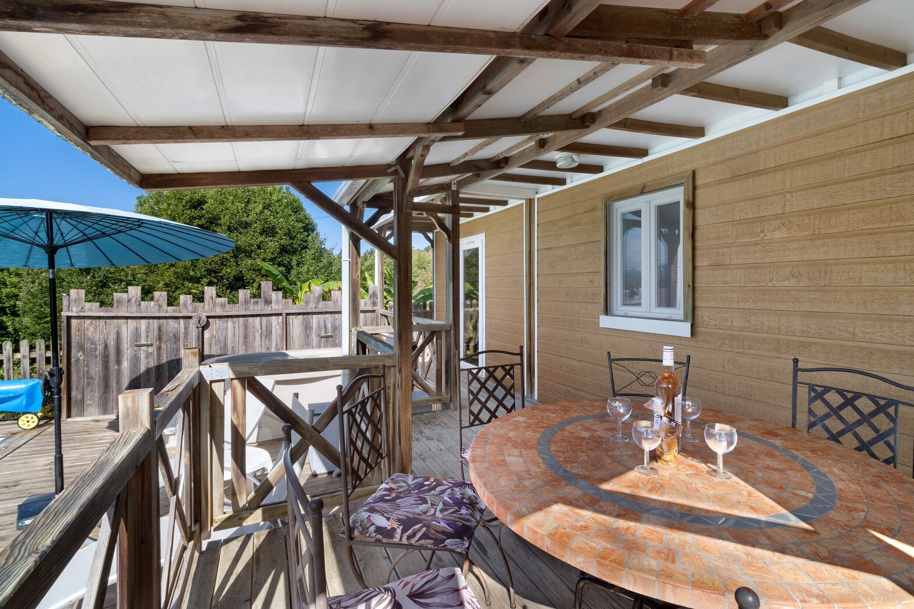 Une terrasse extérieure couverte, avec une table ronde et des chaises, une clôture en bois et un grand parasol.