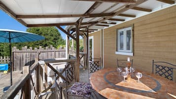 Une terrasse extérieure couverte, avec une table ronde et des chaises, une clôture en bois et un grand parasol.