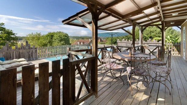 Une terrasse en bois avec un espace salon couvert, une piscine et une vue sur un quartier résidentiel.