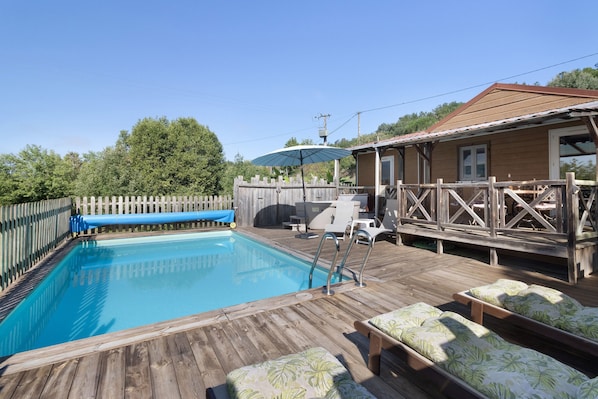 Une terrasse en bois avec une piscine, des chaises longues et un espace couvert comprenant une table et des chaises.