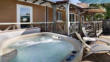 Uma banheira de hidromassagem em um deck de madeira, com cadeiras, cerca de madeira e um edifício com janelas.