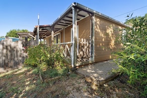 Une structure en bois surmontée d’un toit en métal, entourée d’une clôture en bois, et accessible par un chemin de gravier.