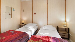 Une chambre avec deux lits simples, des murs en bois, une petite table de chevet avec une lampe et un miroir sur le mur de gauche.