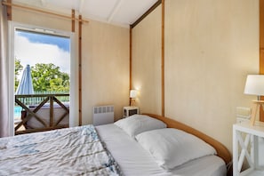 Une chambre d’hôtel avec un lit, une table de chevet, une lampe et une vue sur une piscine et des arbres.