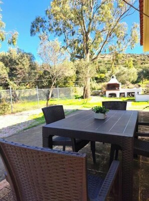 Eine Terrasse im Freien mit Tisch und Stühlen, umgeben von einem Zaun und Bäumen.