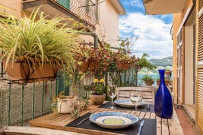 Un balcon avec une table dressée pour deux personnes, des plantes en pot et une vue sur la mer.