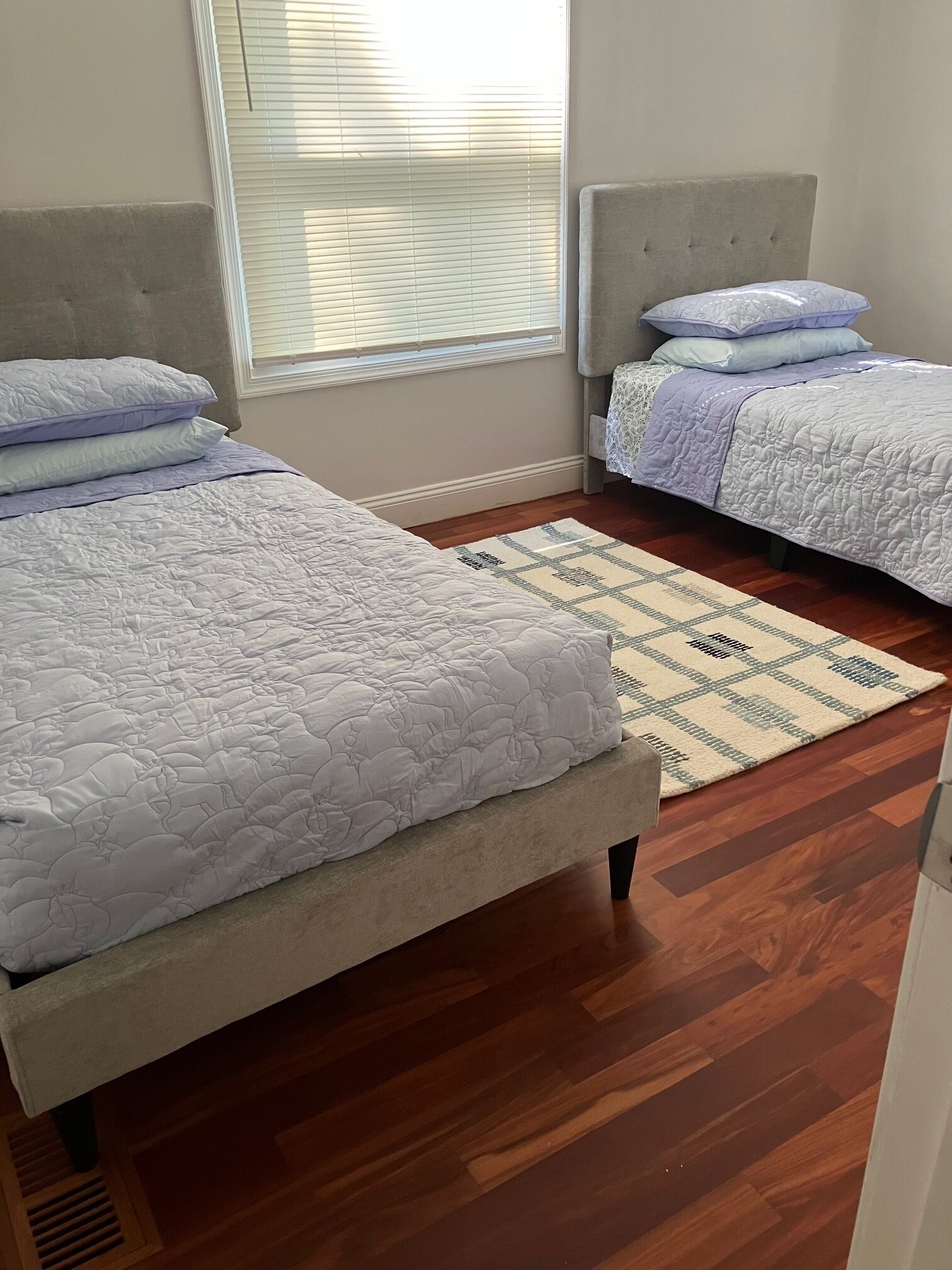 A bedroom with two beds, a patterned rug, and a window with blinds.