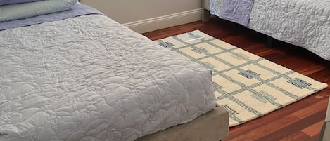 A bedroom with two beds, a patterned rug, and a window with blinds.
