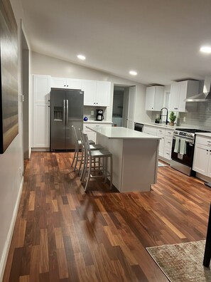Eine moderne Küche mit weißen Schränken, einem Edelstahlkühlschrank, einem eingebauten Backofen und Holzboden.