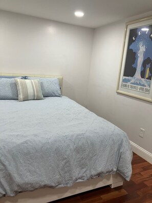 A bedroom with a bed, pillows, a wall-mounted poster, and a wooden floor. - SPACIOUS 4 BEDROOM HOUSE WITH CENTRAL AIR FOR A FAMILY OR GROUP OF ADULTS! (Somers Point)