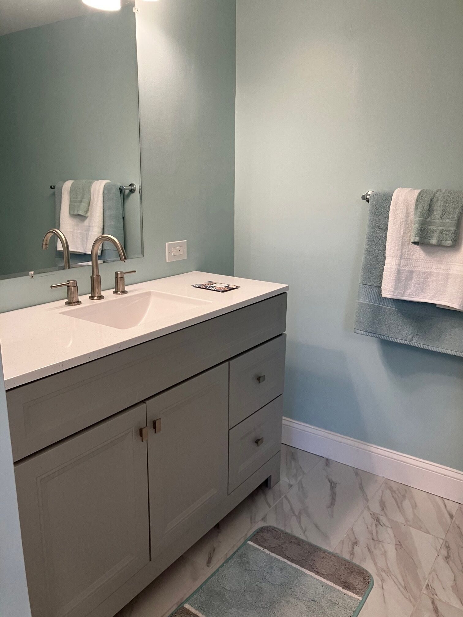 A bathroom with a white sink, a mirror, a towel rack, and a marble floor.