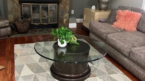 Ein Wohnzimmer mit Glastisch, Kamin, einer Couch und einem gemusterten Teppich.
