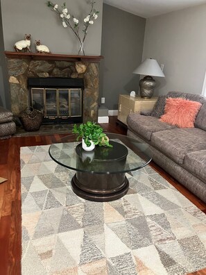 Ein Wohnzimmer mit Glastisch, Kamin, einer Couch und einem gemusterten Teppich.