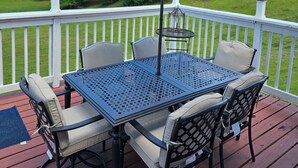 Una terraza con mesa y sillas, una pérgola con sombrilla y vista a un campo cubierto de césped.