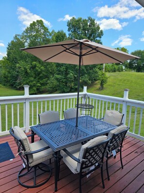 Eine Terrasse mit Tisch und Stühlen, eine Pergola mit Sonnenschirm und Blick auf ein Wiesenfeld.