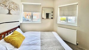 A bedroom with a bed, two windows with blinds, a radiator, and a mirror on the wall. - Contractor Stay | 3 Bedrooms | Long Stays Welcome (Southampton)