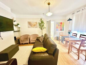 Ein Wohnzimmer mit einer Couch, Sesseln, einem Esstisch und einem an der Wand befestigten Fernseher.