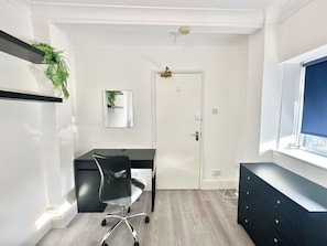 Ein Zimmer mit Schreibtisch, Stuhl und Fenster.
