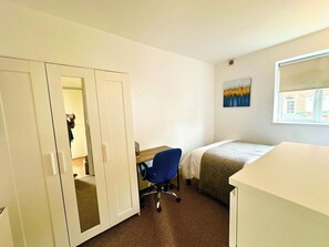 Ein Hotelzimmer mit Bett, Schreibtisch, Stuhl, Kleiderschrank und einem Bild an der Wand.