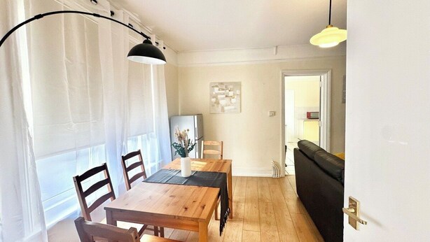A dining area with a wooden table and chairs, a black lamp, and a white curtain. - Contractor Stay | 3 Bedrooms | Long Stays Welcome (Southampton)