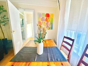 Ein Essbereich mit einem Holztisch, einer Vase mit getrockneten Pflanzen und einem farbenfrohen, abstrakten Gemälde an der Wand.