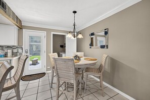 A dining area with a round table, chairs, and a chandelier. - Escape the High-Rise | Gulf Highlands Resort for 6 (Panama City Beach)