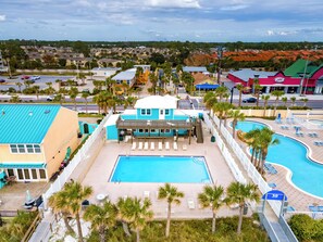 Ett hotellkomplex med en central pool, ett avskärmat område med solstolar och utsikt över det omgivande bostadsområdet.