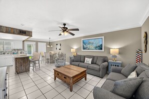 A modern living room with a grey sofa, a wooden coffee table, and a dining area with a white table and chairs. - Escape the High-Rise | Gulf Highlands Resort for 6 (Panama City Beach)