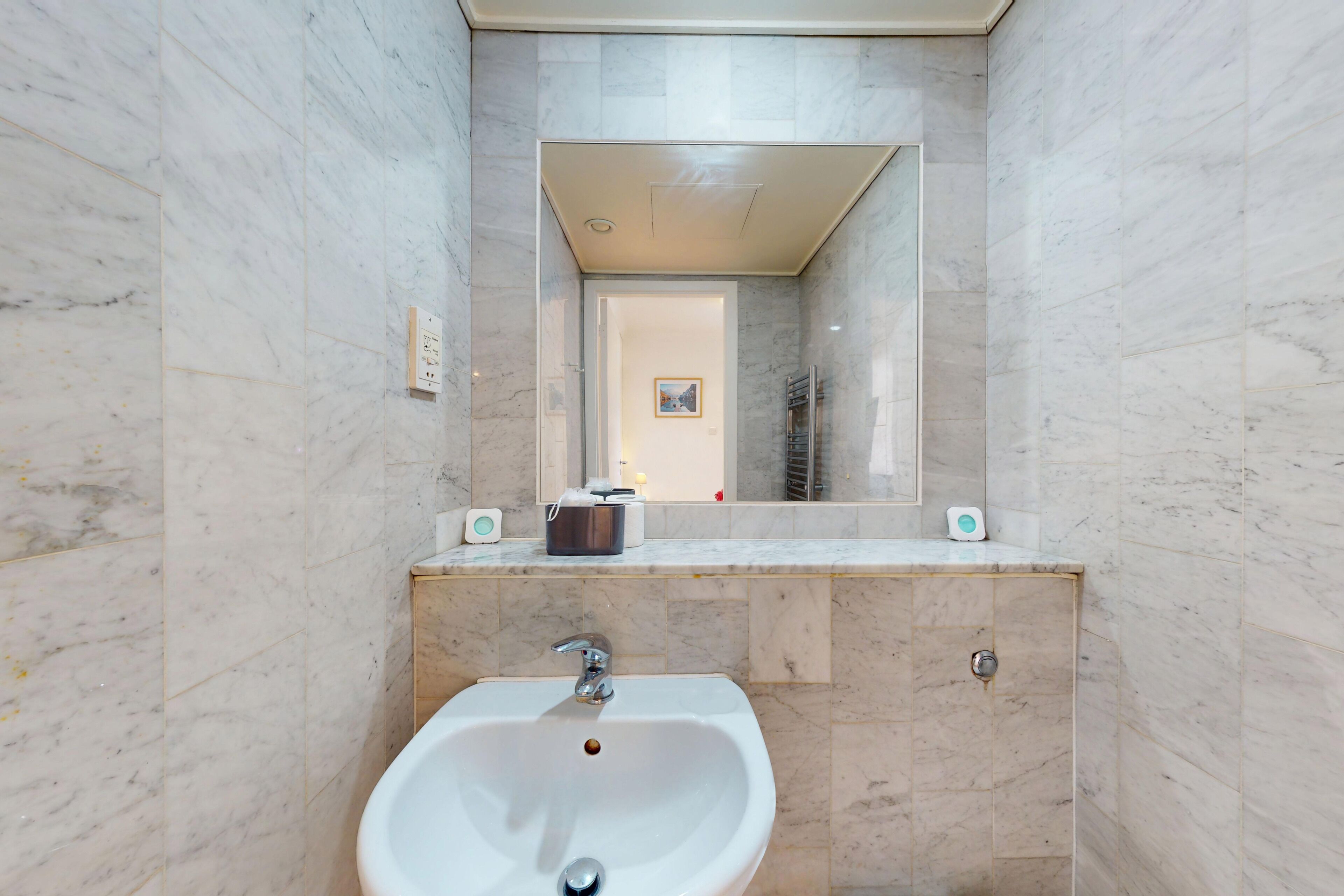 A bathroom with a marble wall, a sink with a faucet, a mirror, and a towel rack.