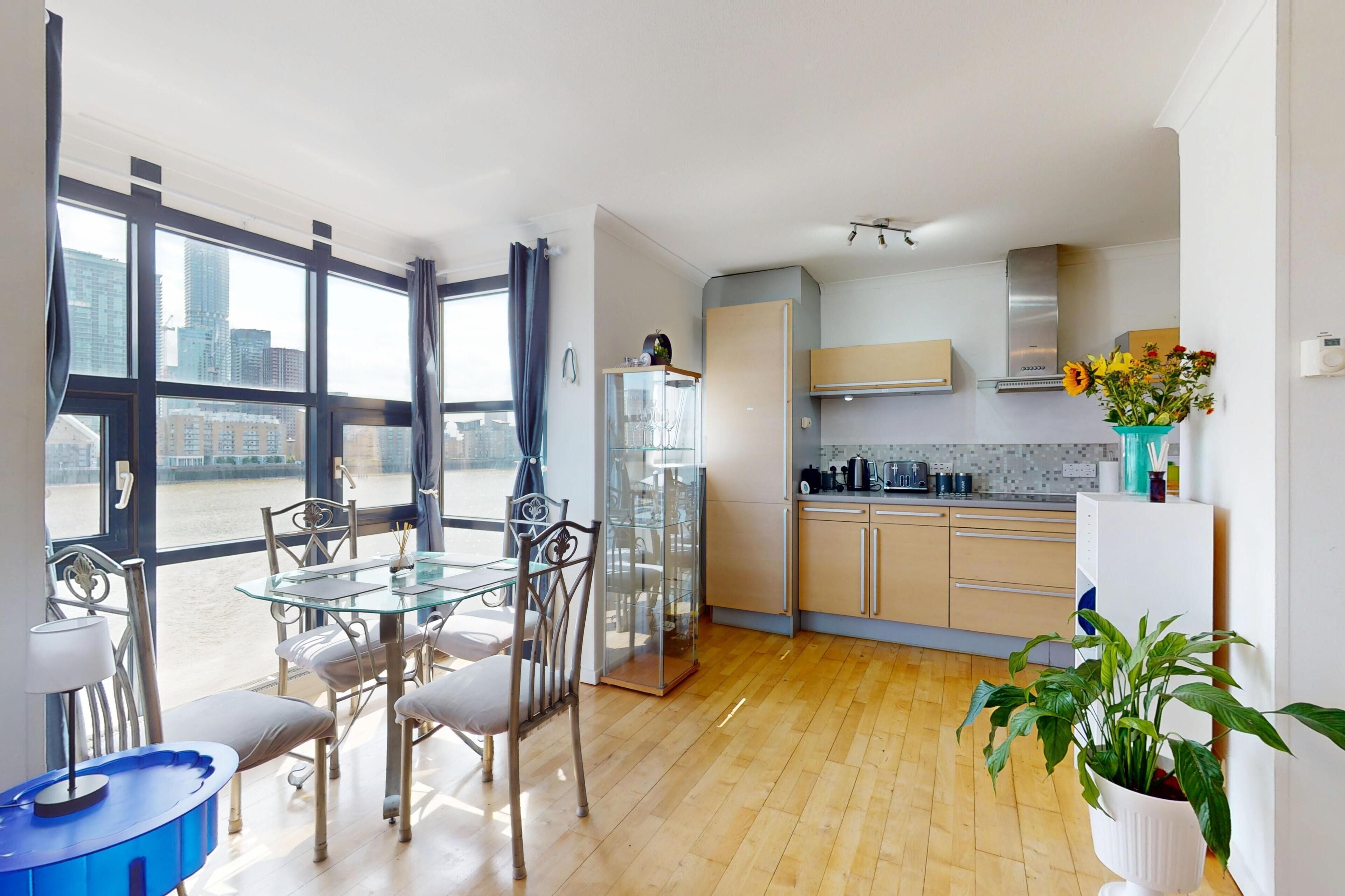 A modern kitchen with a glass dining table, chairs, and a view of the city through large windows.